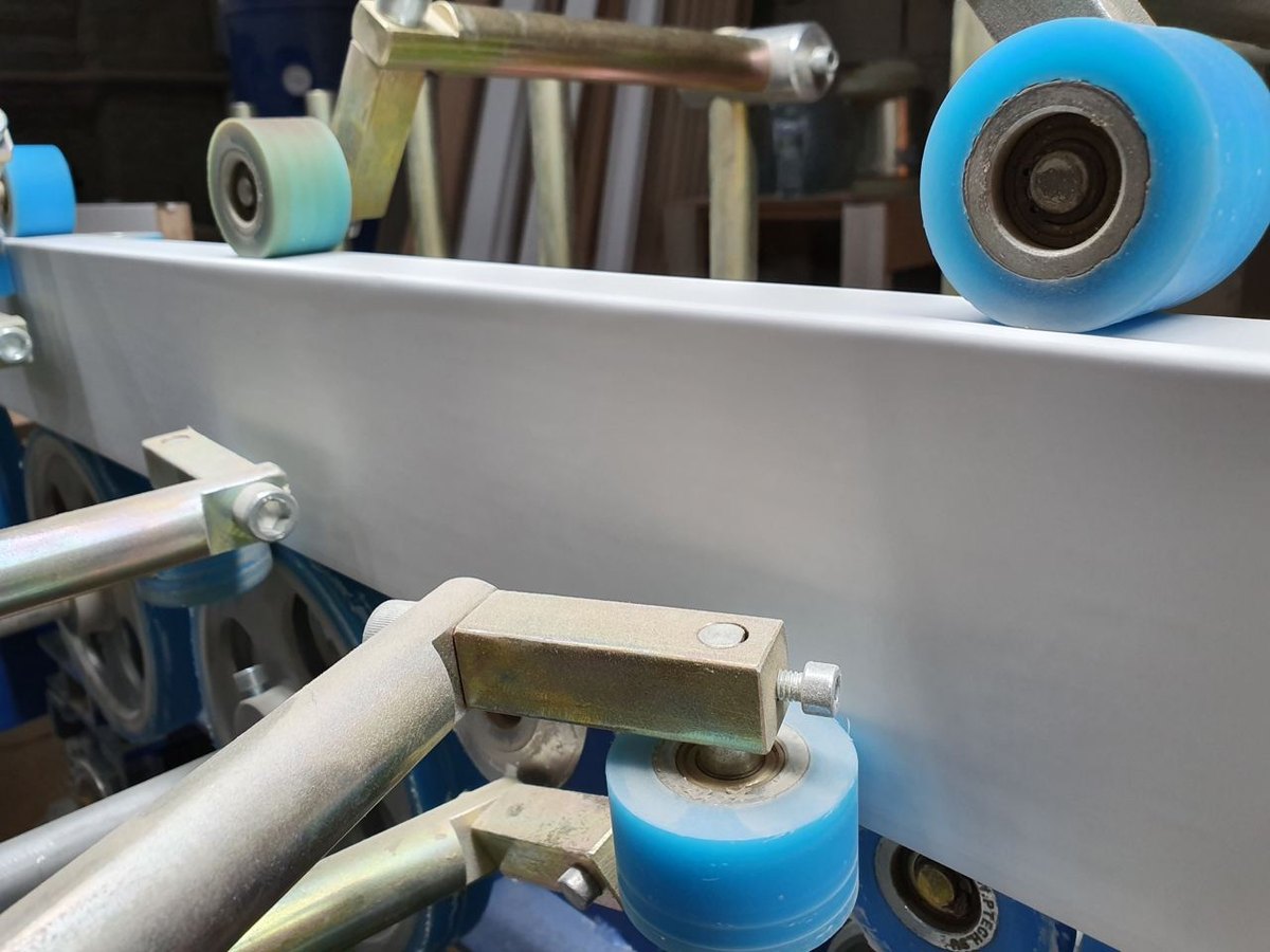 Profile wrapping line applying decorative PVC film to a linear profile with pressure rollers
