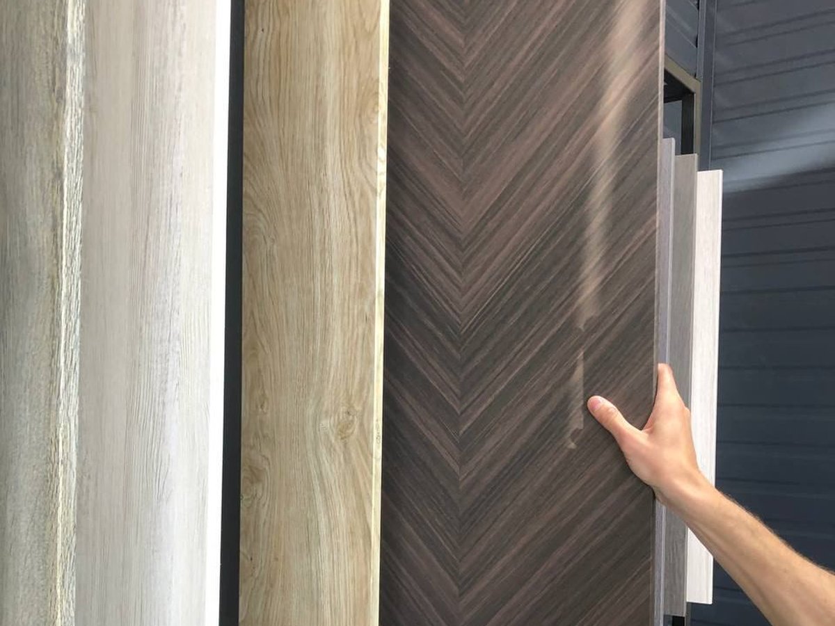 Hand selecting a dark woodgrain chevron PVC film decor among light oak sample panels